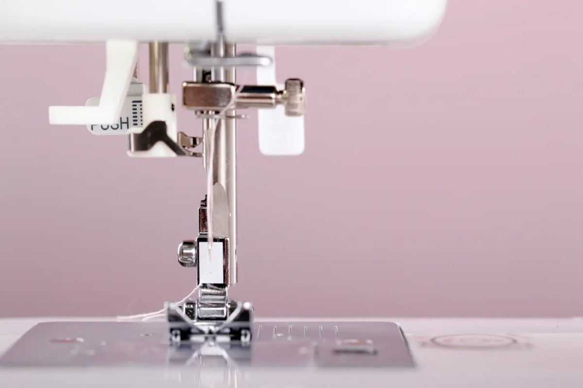 Close-up of a sewing machine needle and presser foot on a pink background
