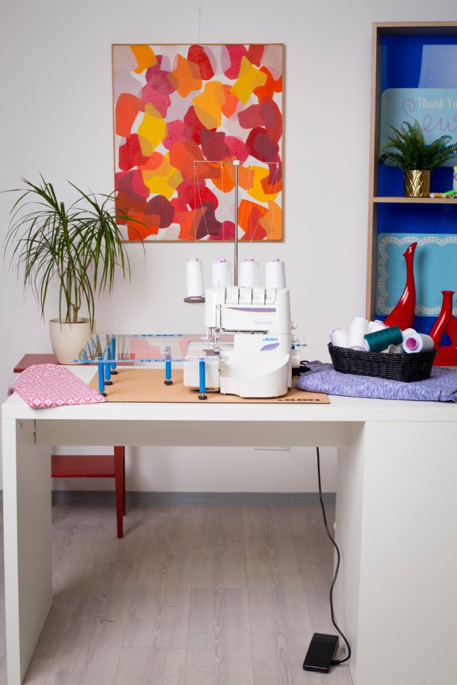 Juki MO-1000 on a white desk with an extended work space and basket of thread