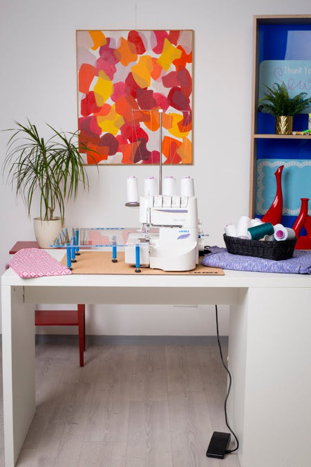 Juki MO-1000 on a white desk with an extended work space and basket of thread