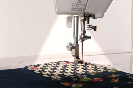 Juki TL-2000Qi Sewing machine needle stitching fabric on a white background